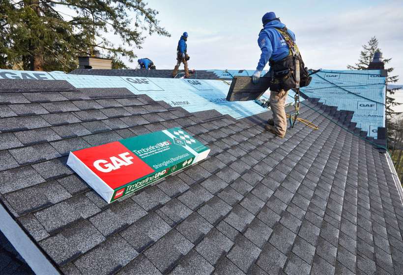Condition One crew member carrying a bundle of GAF Timberline shingles across a roof